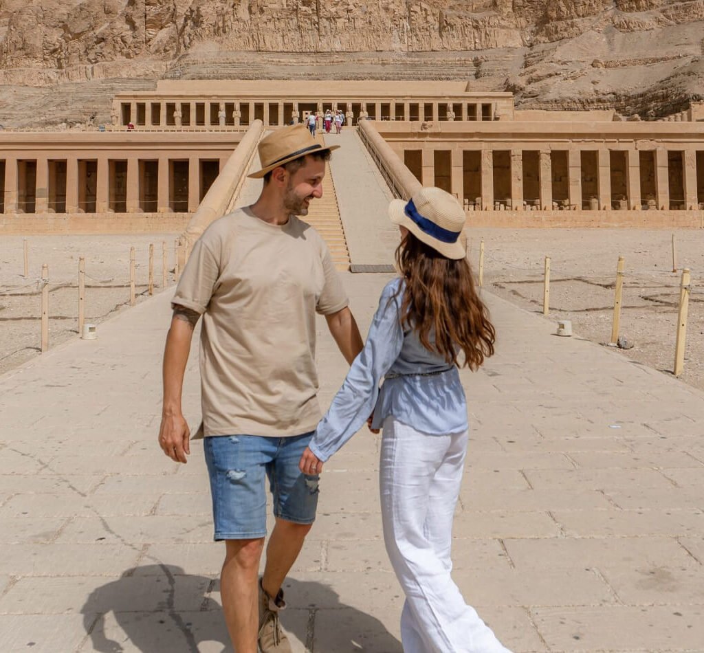 A happy couple holding hands in front of Hatshepsut Temple in Luxor during their Egypt 14-day itinerary, a top highlight of Egypt Christmas Tours.