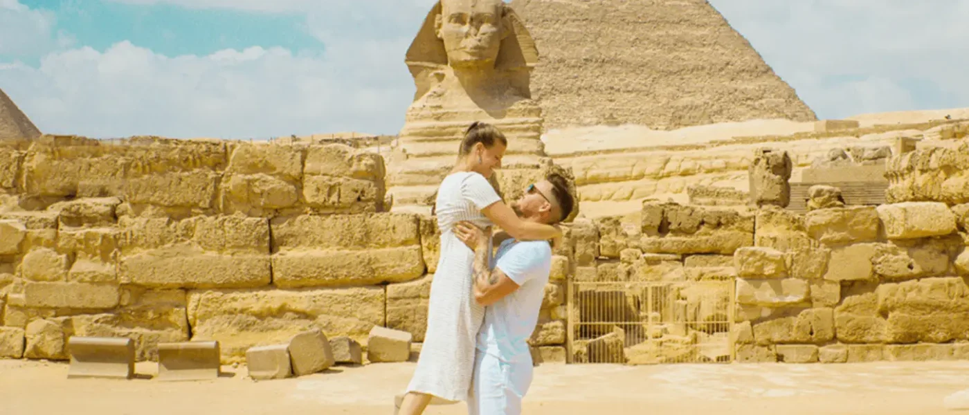 A man lifting a woman in a white dress in front of the Great Sphinx and a pyramid at the Giza Plateau, Egypt
