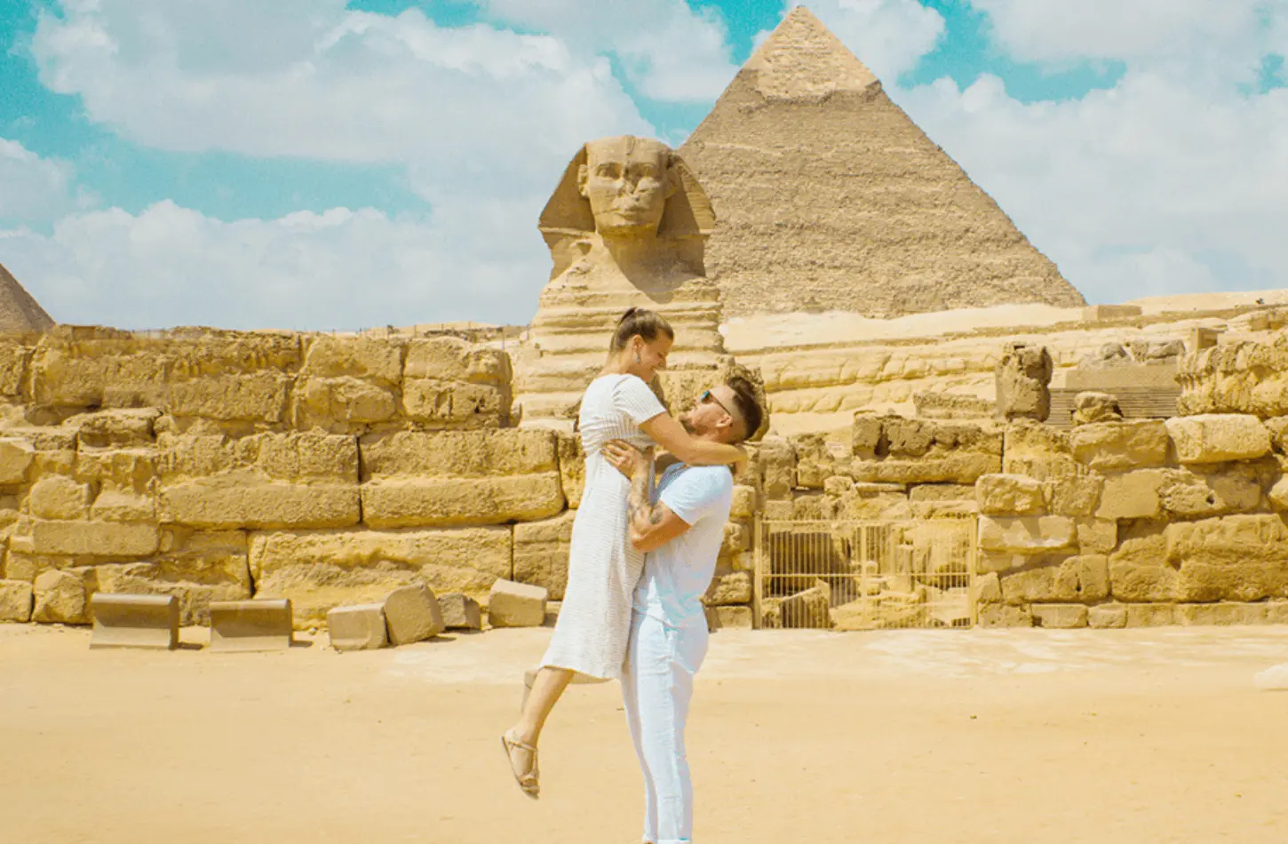 A man lifting a woman in a white dress in front of the Great Sphinx and a pyramid at the Giza Plateau, Egypt