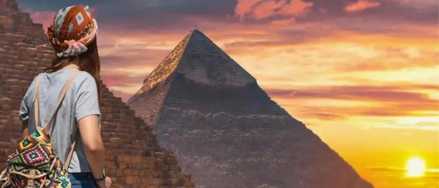 Egypt travel cost per day can vary while visiting iconic sites like the Great Pyramids of Giza, shown here at sunset with a female traveler overlooking the ancient stone structures and a tour bus in the desert.