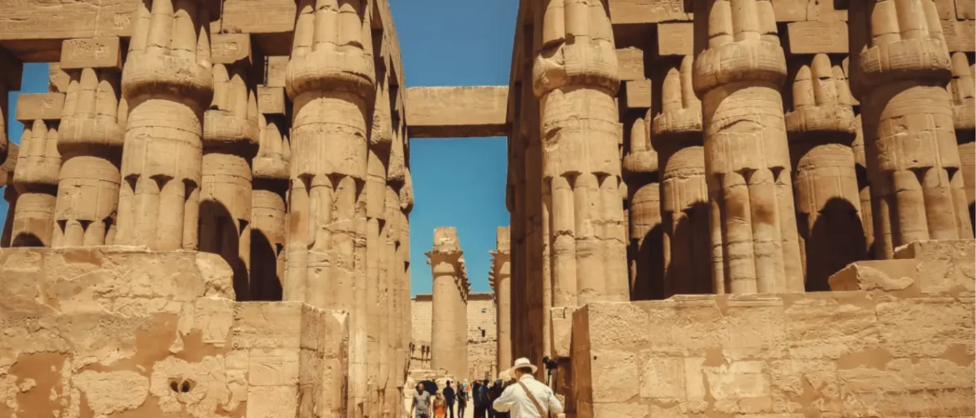 Tourists walking through the massive stone columns of the Great Hypostyle Hall at Karnak Temple Complex in Luxor, Egypt.