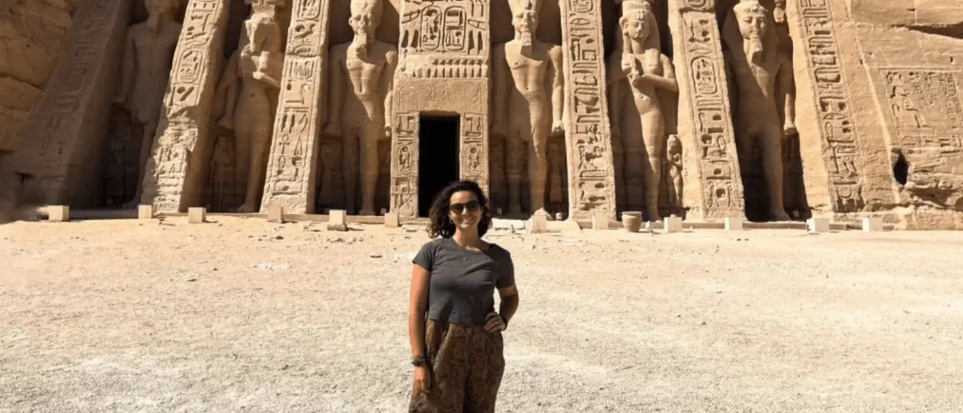A woman standing in front of the Temple of Nefertari at Abu Simbel, featuring six large standing statues of Ramses II and Queen Nefertari