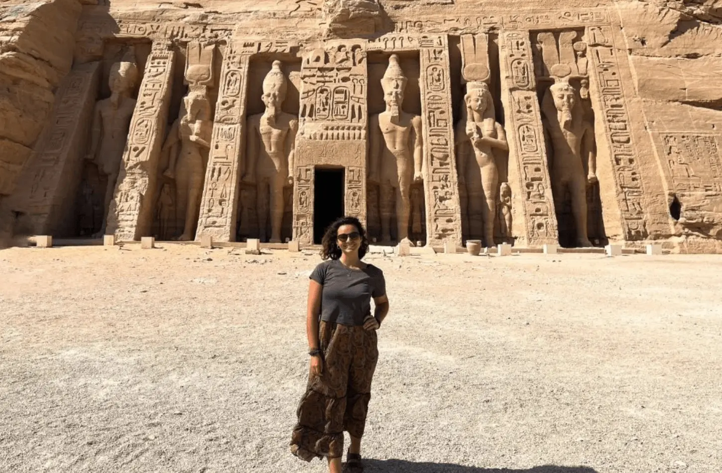 A woman standing in front of the Temple of Nefertari at Abu Simbel, featuring six large standing statues of Ramses II and Queen Nefertari