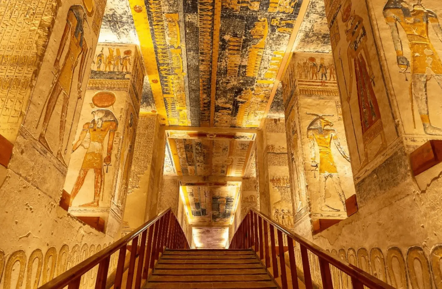 Interior view of the Tomb of Ramses VI in Luxor, Egypt, featuring pillars and ceilings covered in vibrant yellow and blue Ancient Egyptian paintings and hieroglyphics.