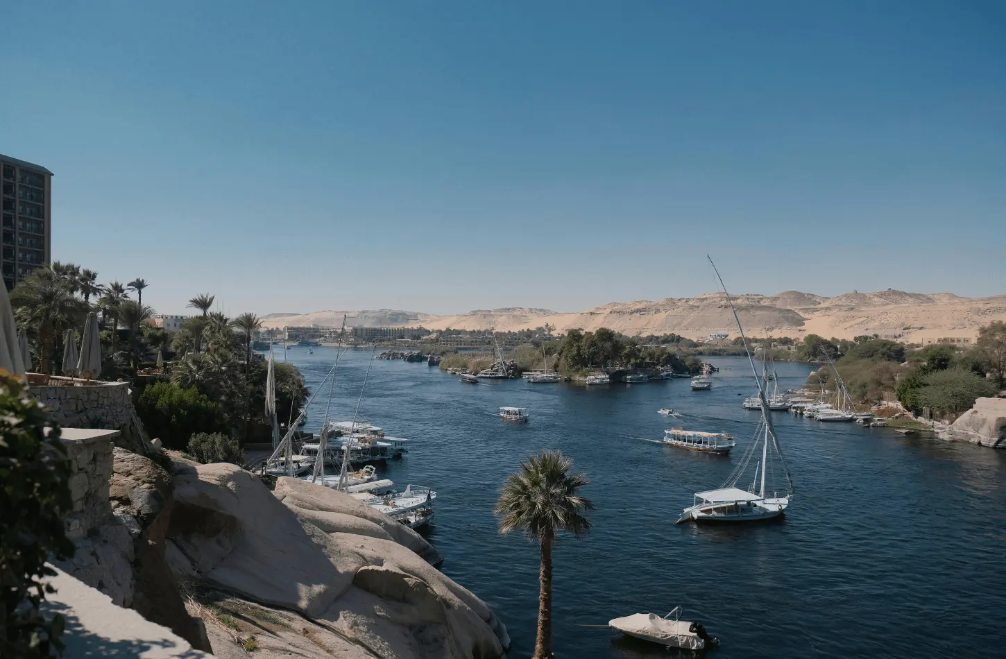A scenic view of the Nile River in Aswan with traditional felucca boats and desert hills, perfect for a guide on how to travel Egypt on a budget.