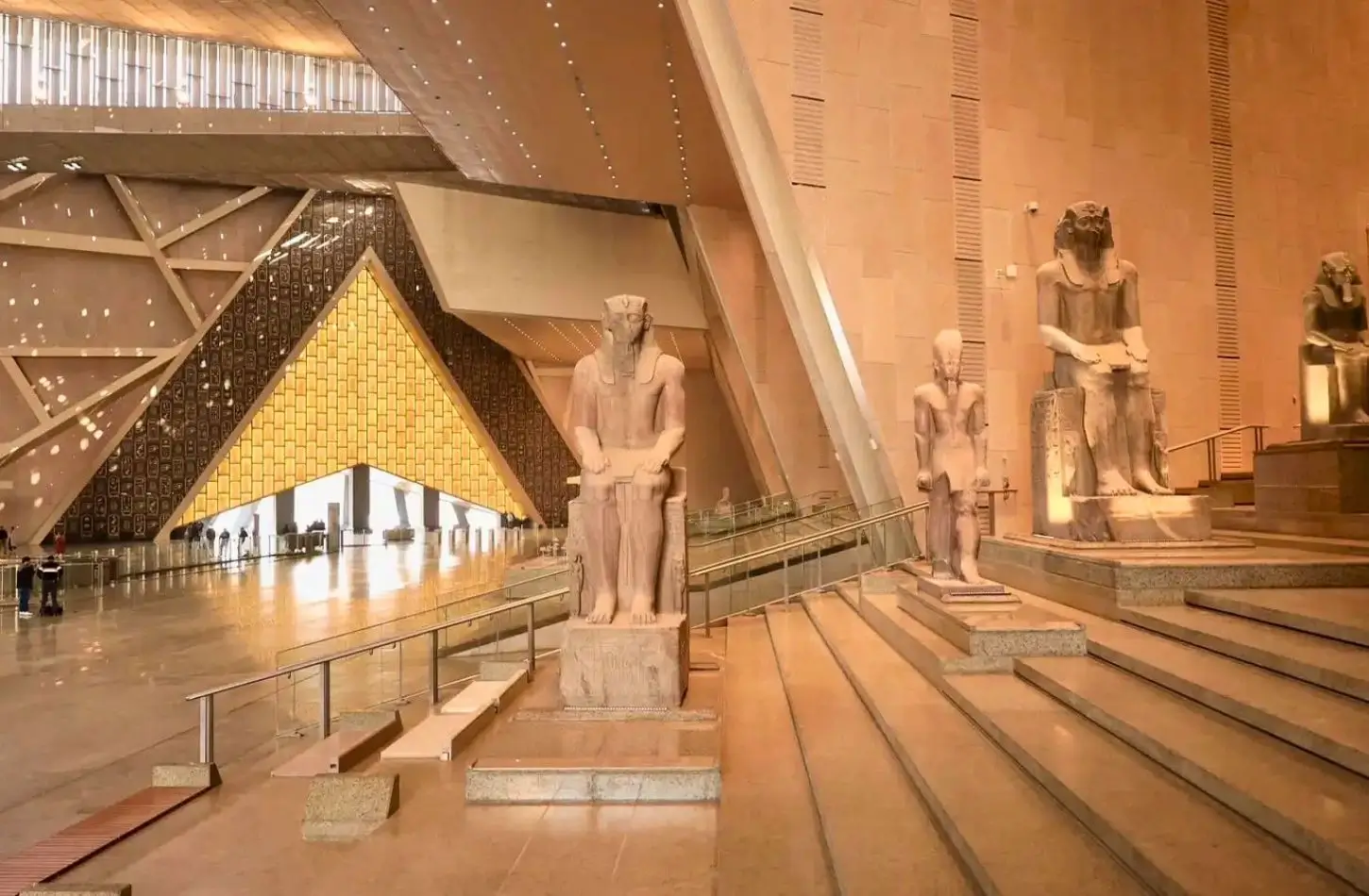 Large ancient Egyptian pharaoh statues lined up on the Grand Staircase inside the modern, sunlit atrium of the Grand Egyptian Museum.