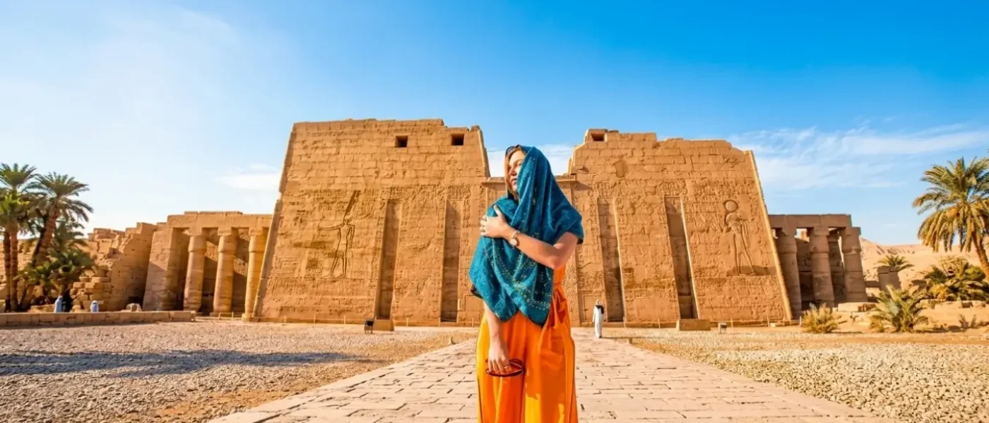 A female traveler wearing a blue scarf stands in front of an ancient pharaonic temple in Luxor, showcasing the ideal weather for visiting Egypt in October.