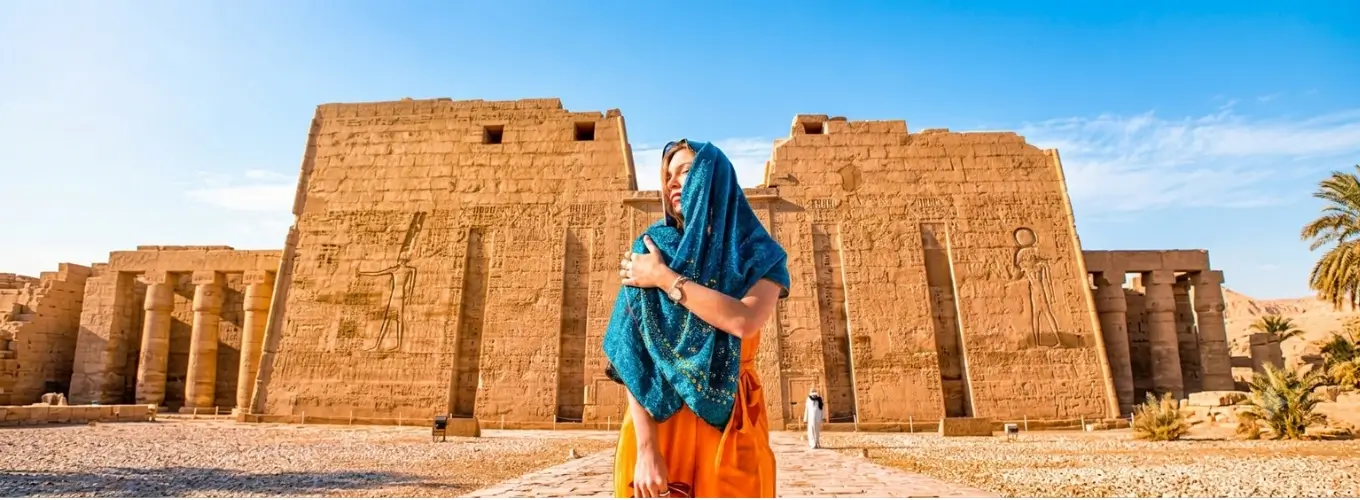 A female traveler wearing a blue scarf stands in front of an ancient pharaonic temple in Luxor, showcasing the ideal weather for visiting Egypt in October.