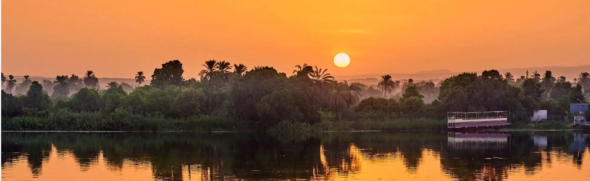 Golden hour sunset over the Nile River with palm trees and a boat, showcasing scenic routes for how to get around Egypt.