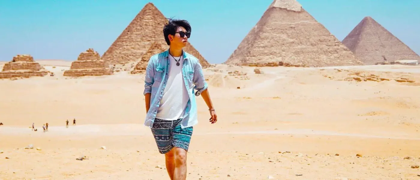 A male traveler walking through the desert landscape of Giza with the iconic pyramids in the background, highlighting the top things to do in Egypt.