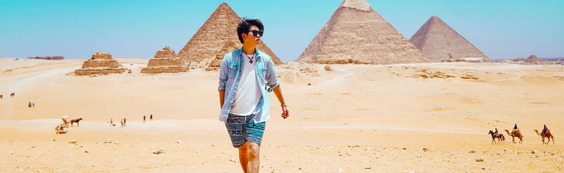 A male traveler walking through the desert landscape of Giza with the iconic pyramids in the background, highlighting the top things to do in Egypt.