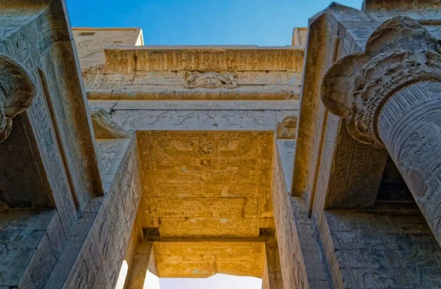Intricate hieroglyphic carvings and towering stone columns framing the doorway of Edfu Temple.