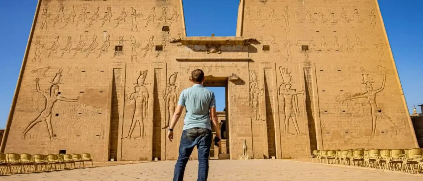 A traveler looking up at the towering facade and ancient carvings of Edfu Temple.
