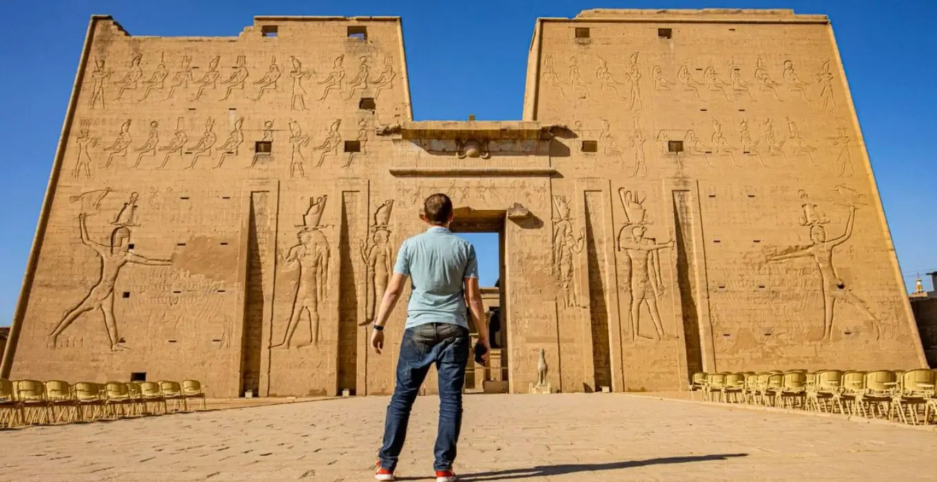 A traveler looking up at the towering facade and ancient carvings of Edfu Temple.