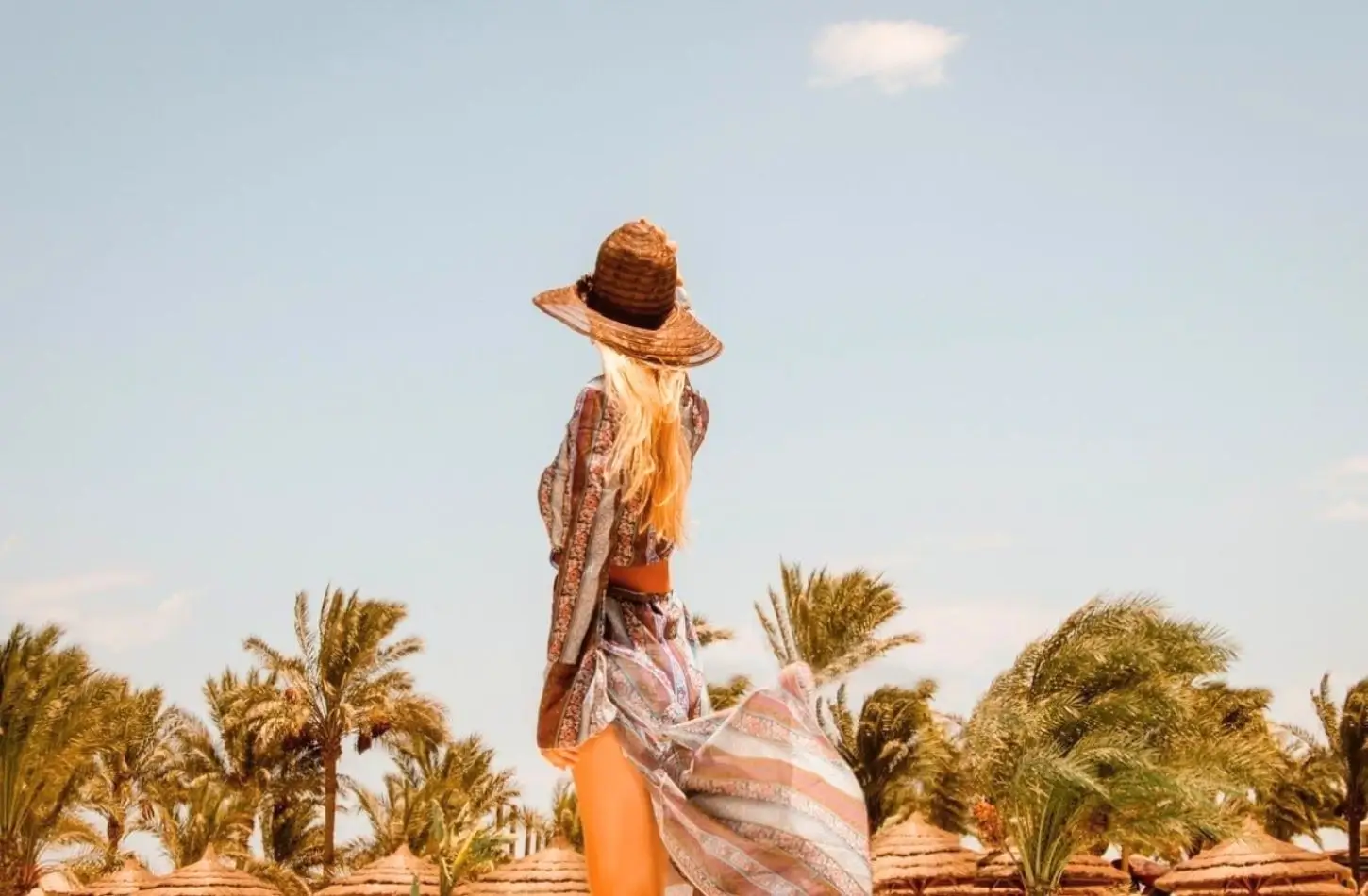 Woman enjoying a sunny resort vacation surrounded by palm trees and thatched beach umbrellas in Egypt in February.